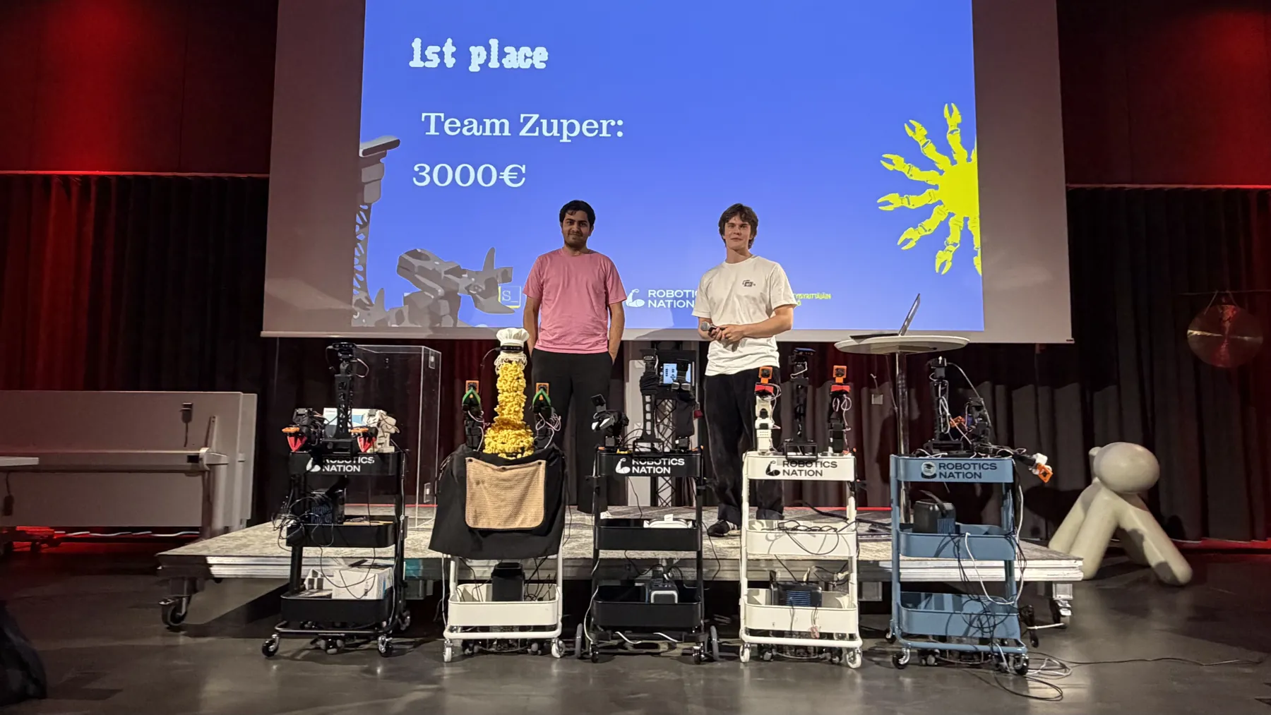 Zuper on stage in front of the first place slide, with the XLeRobots lined up
